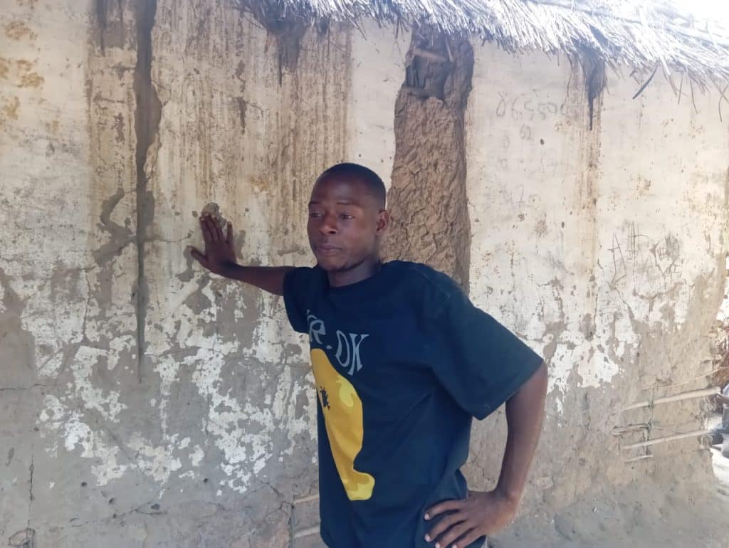 A young man from Mozambique Island stands beside a weathered mud wall of a traditional house, resting his hand against it while looking thoughtfully ahead, representing unemployment and the search for work opportunities.